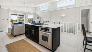 A modern kitchen with a central island, black cabinetry, and a dining area with a white railing. - Easy Livin' | 1040 ft from the beach | Private Pool, Hot Tub | Duck (Duck)