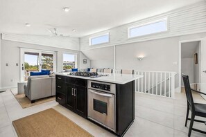 Une cuisine moderne dotée d’un îlot central, de meubles de couleur noire et d’un coin repas agrémenté d’une rambarde blanche.
