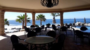 Un espacio de estar al aire libre cubierto con mesas y sillas, con vistas a una playa y al océano.
