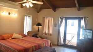 Un dormitorio con cama, ventilador de techo, televisor y balcón con cortinas.