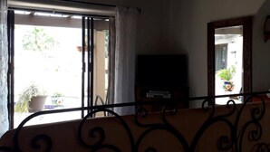 Huone, jossa on parveke, jalustalla oleva televisio ja ruukussa oleva kasvi parvekkeella.