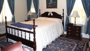 Une chambre à coucher avec un lit en bois, des rideaux bleus, un tableau encadré au mur et une table de chevet avec une lampe.