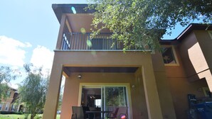 Un bâtiment à deux étages doté d’un balcon, d’une terrasse avec des chaises et d’une porte-fenêtre coulissante donnant sur l’intérieur.