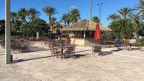Un espace extérieur aménagé avec des tables et des chaises, une structure à toit de chaume et des palmiers.