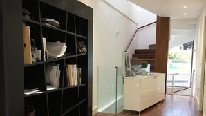 Un intérieur moderne avec un plancher en bois, une étagère noire, un meuble blanc et un escalier menant à un balcon.