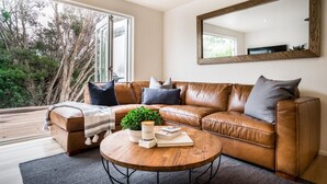 Un salon moderne avec un canapé en cuir, une table basse ronde et un grand miroir au mur.