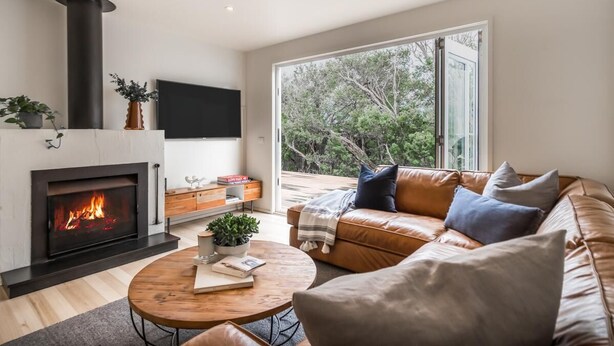 Un salon moderne avec une cheminée, un canapé en cuir et une grande fenêtre donnant sur la forêt.