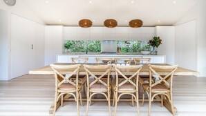 Une cuisine moderne dotée d’un îlot central, de meubles blancs et d’un coin repas avec des chaises en osier.