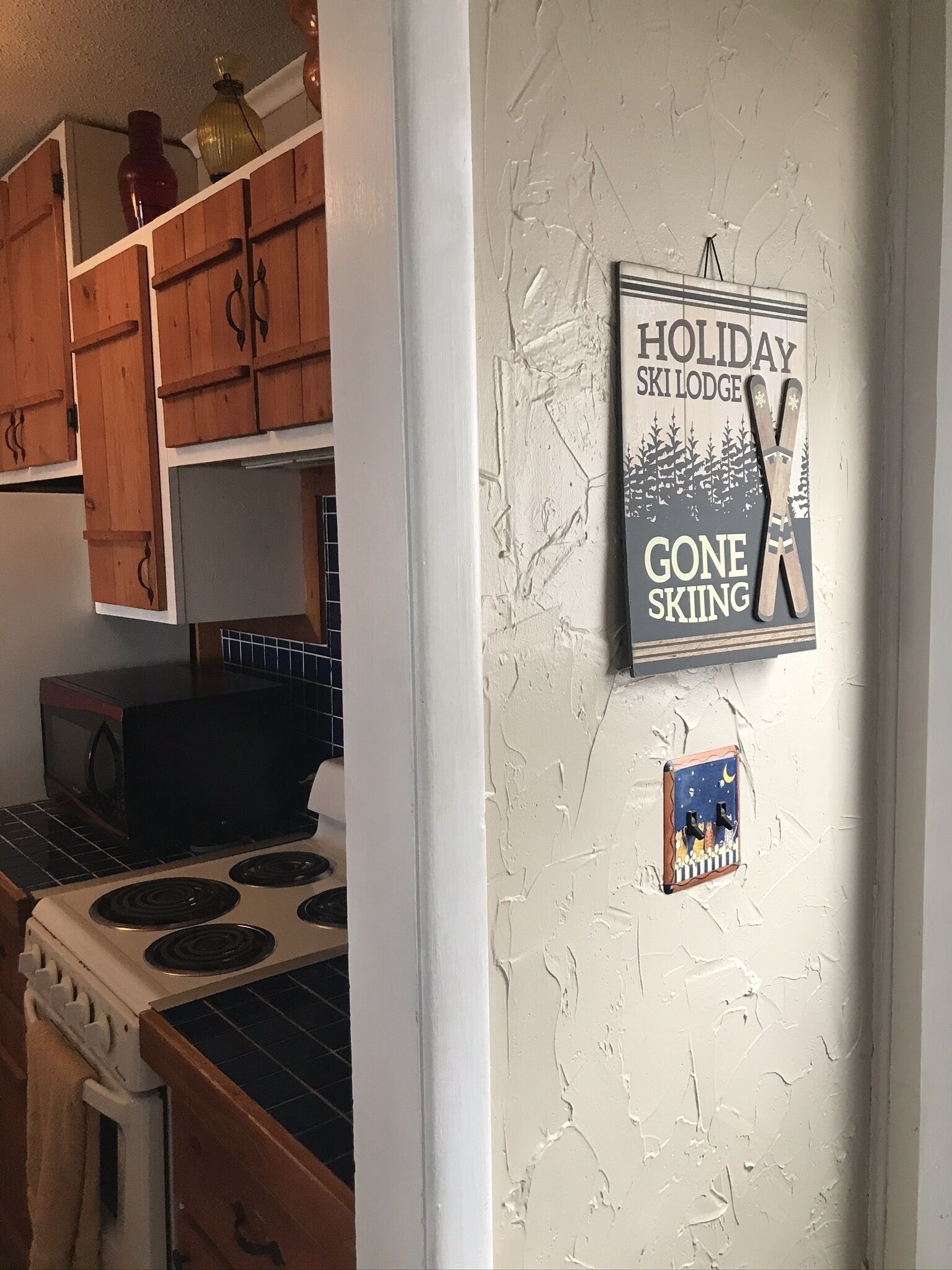 Cuina amb armaris de fusta, forlla i microones. Al mur hi ha un cartell que diu: "Holiday Ski Lodge Gone Skiing".