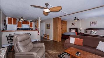 Ein kompakter Wohnbereich mit Küchenzeile, Essbereich, Schlafzimmer mit Bett und Nachttisch sowie Sitzgelegenheit mit Sofa und Sessel.