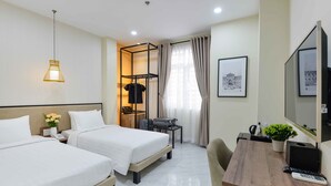 A hotel room with two beds, a desk with a computer, a TV, and a small table with a plant.