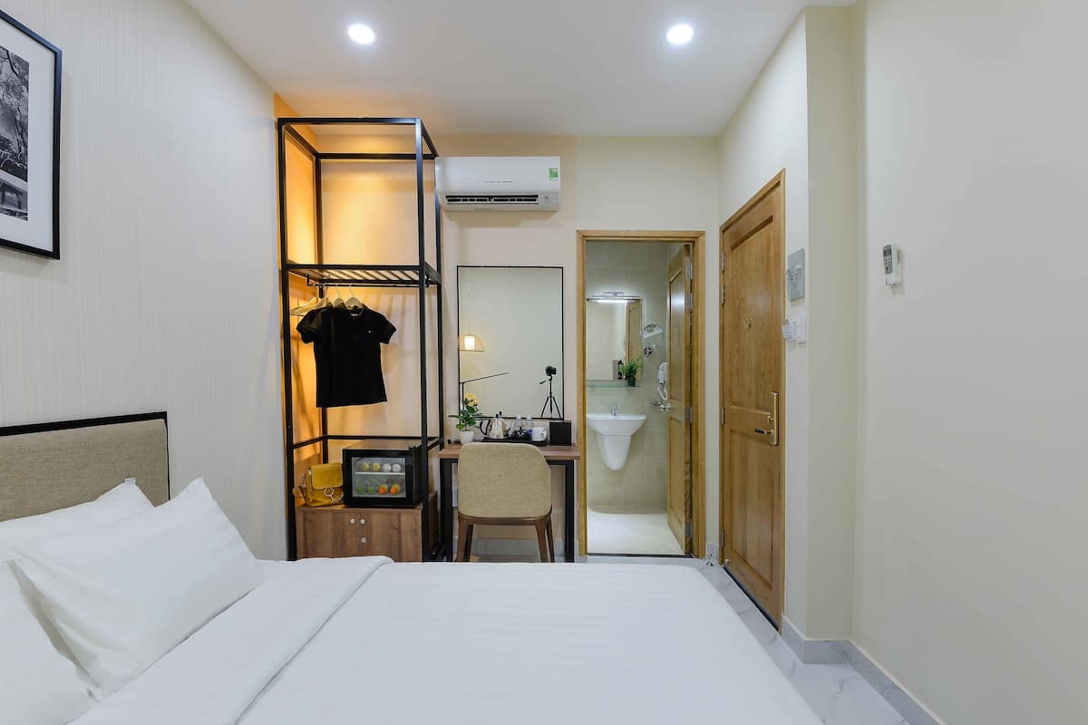 Hotelkamer met een bed, een bureau met stoel, een kleine tafel met lamp, een spiegel en een zichtbare badkamer door een geopende deur.