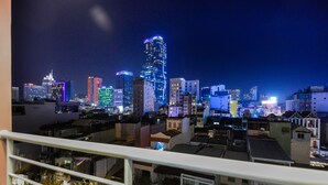 A nighttime cityscape with illuminated buildings, a balcony with a railing, and a view of the urban environment.