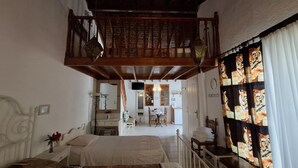 Ein Schlafzimmer mit einem Bett, einem kleinen Tisch und einem Stuhl. Ein Balkon mit Holzgeländer und Blick ins Freie ist vorhanden.