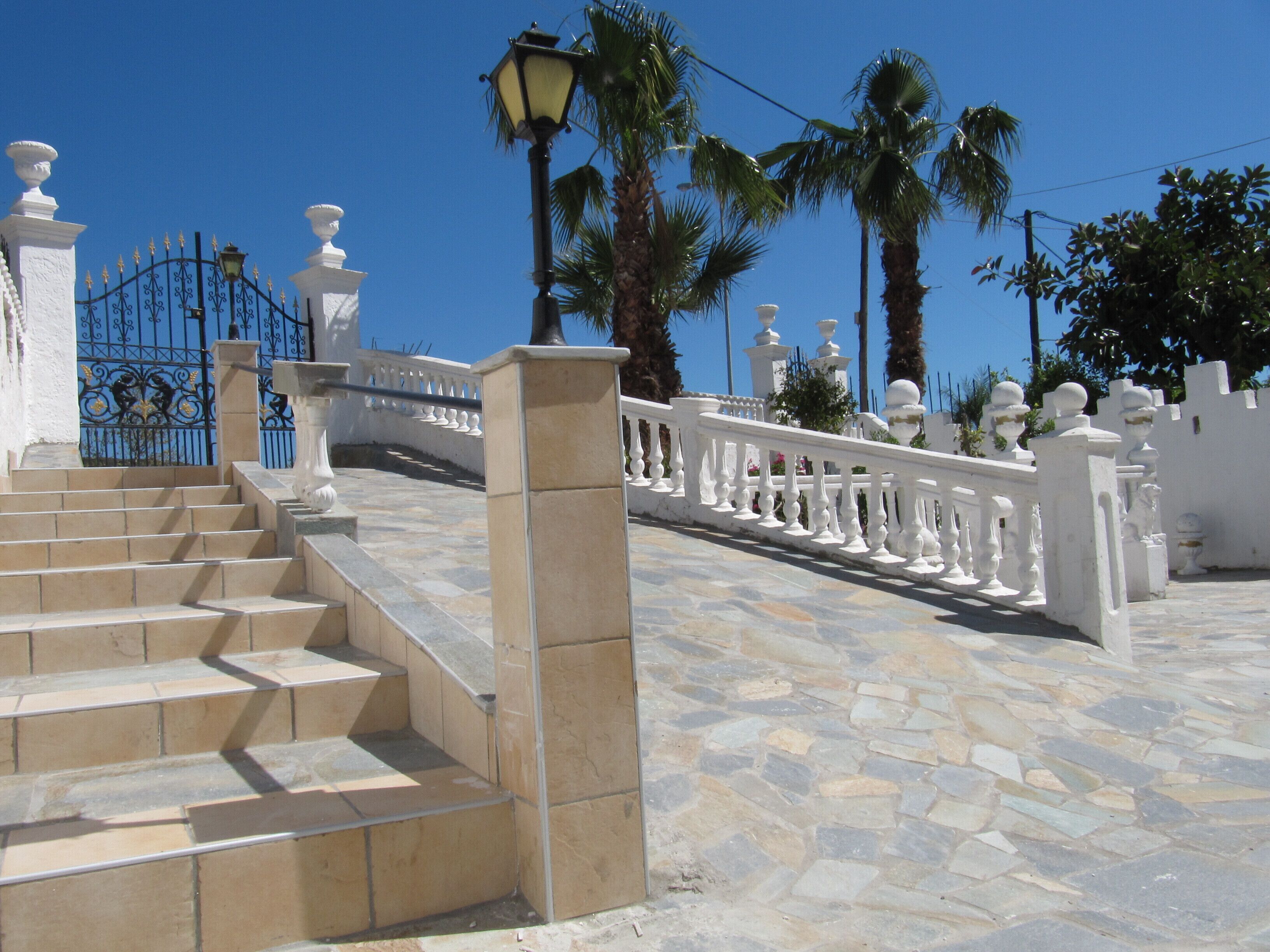 A stone staircase leading up to a white gate with a wrought iron fence.