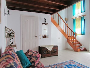 Une pièce avec un escalier en bois, une porte blanche, un canapé à motifs floraux, une commode en bois et un tapis à motifs.