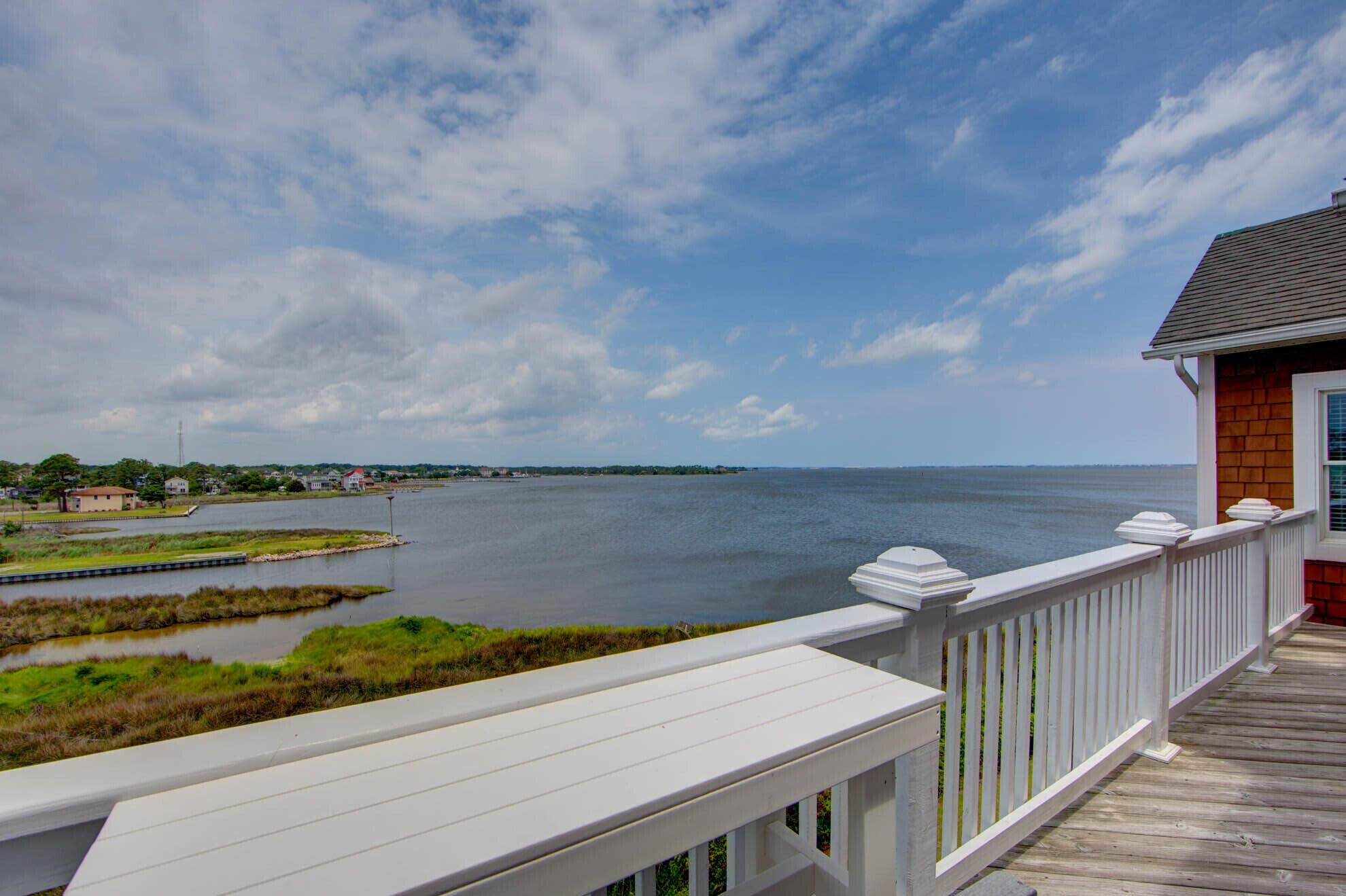 A wooden deck with a view of a calm body of water and distant shoreline houses.