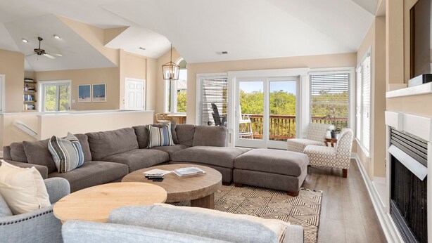 A spacious living room with a sectional sofa, a round coffee table, and a fireplace. There is a balcony with a view of the outdoors. - Banks Retreat: Private Pool, Hot Tub, Dog-friendly, 700 feet to Beach Access (Corolla)