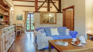 Un accogliente soggiorno con un divano blu, travi in legno, una parete in pietra e un'area pranzo con tavolo e sedie.
