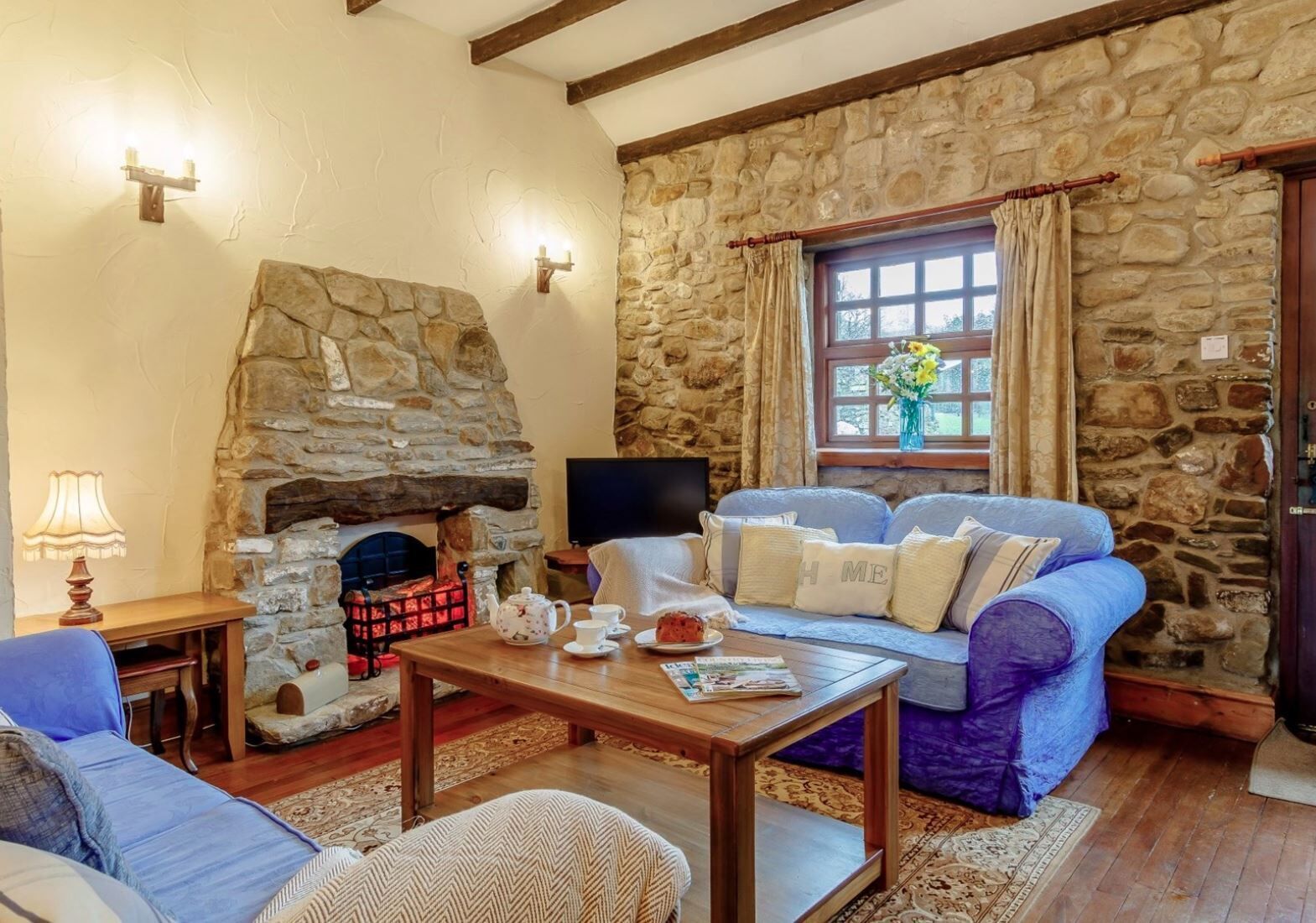A cozy living room with a stone fireplace, a comfortable sofa, a wooden coffee table, and a television.