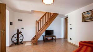 Un vaste espace de vie agrémenté d’un escalier en bois, d’un téléviseur posé sur un meuble et d’une décoration en forme de roue de voilier.