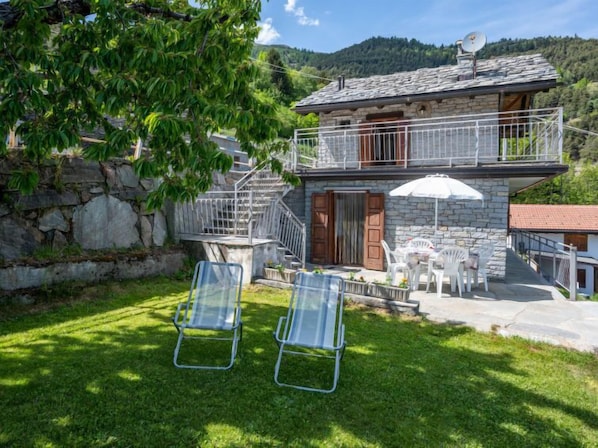 Une maison en pierre dotée d’un balcon, d’un espace extérieur aménagé pour s’asseoir et d’un escalier menant à un étage supérieur.