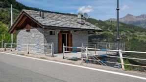 Un bâtiment en pierre avec une porte en bois et une antenne parabolique, entouré d’une clôture en métal et d’un lampadaire.