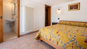 Une chambre à coucher comprenant un lit, une table de chevet, une commode, un radiateur et une salle de bain avec un lavabo et un miroir.