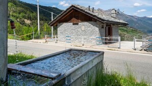 Un bâtiment en pierre avec un toit en bois, une porte en métal et une chaîne de montagnes en arrière-plan.