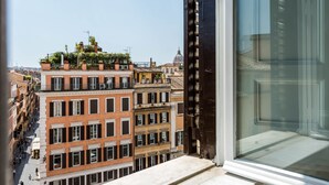 Une vue depuis une fenêtre donnant sur une rangée d’immeubles à plusieurs étages, dotés de balcons, dont certains sont ornés de plantes.