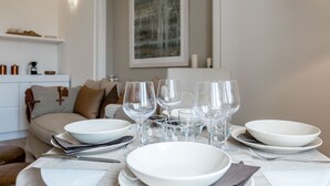 Une table à manger dressée avec de l’assiette blanche, des bols et des verres à vin, avec un canapé et une œuvre d’art en arrière-plan.