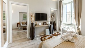 Une chambre d’hôtel moderne équipée d’un lit, d’une table de chevet, d’une télévision et d’une grande fenêtre donnant sur l’extérieur.
