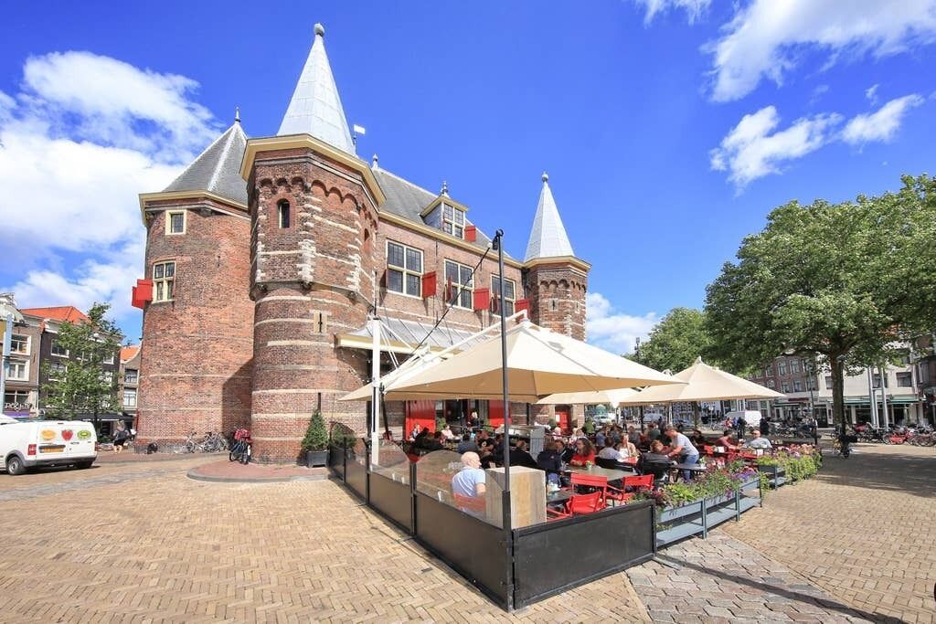 A historic building with brick walls and conical roofs, surrounded by outdoor seating areas with umbrellas.