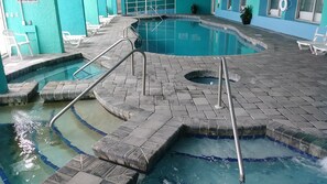 Ein Schwimmbad mit gefliestem Sonnendeck, einem Whirlpool und Liegestühlen.