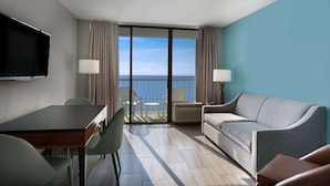 Habitación de hotel con balcón, televisor, sofá, mesa y dos sillas.