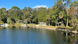 Un entorno tranquilo junto al lago, con un pequeño muelle, un bote y un edificio rodeado de árboles densos.