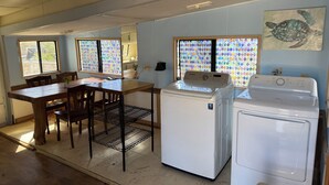 Cocina compacta con una mesa y sillas de madera, dos lavadoras blancas y un ventanal con vidrieras de colores.