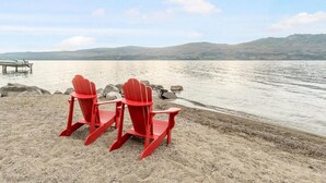Two red Adirondack chairs on a sandy beach with a calm lake and distant mountains. - Barona Beach Lakefront Luxury in front of world class wineries (West Kelowna)