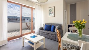 Ein modernes Wohnzimmer mit einer Couch, einem Esstisch und Blick auf die Stadt durch große Fenster.