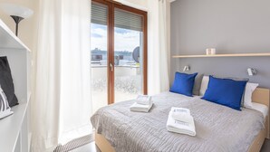 Ein Hotelzimmer mit Bett, einem Vorhangfenster, einem Regal mit Tasse und einem Handtuch auf dem Bett.