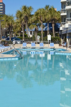 Ein Swimmingpool mit blau-weißen Liegestühlen, Palmen und blauem Himmel.