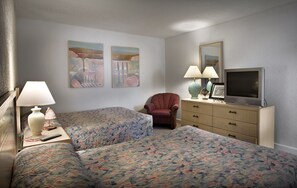 Ein Hotelzimmer mit zwei Betten, einem Fernseher, einem Sessel und Bildern an der Wand.