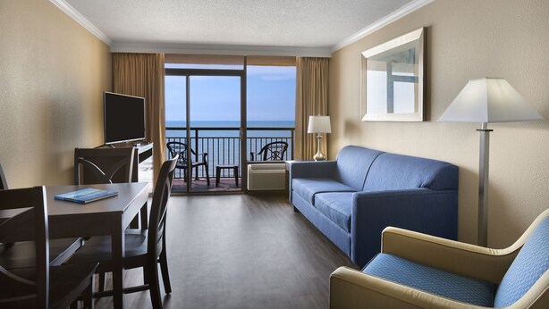 A hotel room with a balcony, a sofa, a chair, a desk, and a TV. - Beautiful Oceanfront Suite w/ Great View + Official On-Site Rental Privileges (Myrtle Beach)
