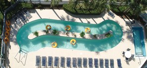 An aerial view of a swimming pool with multiple lanes, surrounded by lounge chairs and sunbeds, with a palm tree and a small island in the center. - Ocean View 2 Bedroom at Exciting Resort + Official On-Site Rental Privileges (Myrtle Beach)