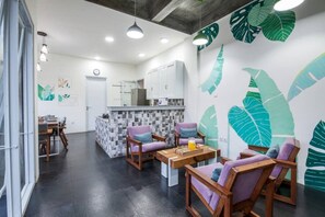 A modern kitchen with a tiled backsplash, wooden cabinets, and a central island. There are two wooden chairs with cushions and a small table with a tray and a glass of orange juice. The walls are decorated with large leaf patterns. - Modern, Deluxe Room with pool view #2 (Mengwi)