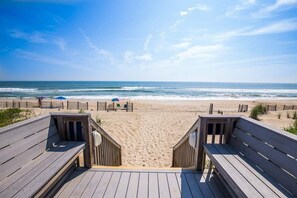 Ein Holzsteg führt zu einem Sandstrand mit freiem Blick auf den Ozean.