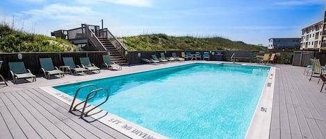 Una piscina rectangular con un deck de madera alrededor, equipada con sillas de descanso y un letrero de seguridad.