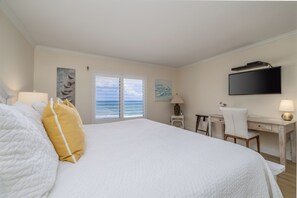 A hotel room with a bed, a desk, a chair, a TV, and a window with a view of the ocean.