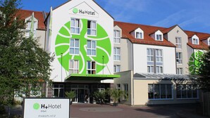 Edificio di un H+Hotel con il logo verde caratteristico, numerose finestre e un tetto in tegole rosse.