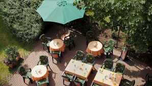 Una terrazza esterna con tavoli e sedie, alcune coperte da ombrelloni.
